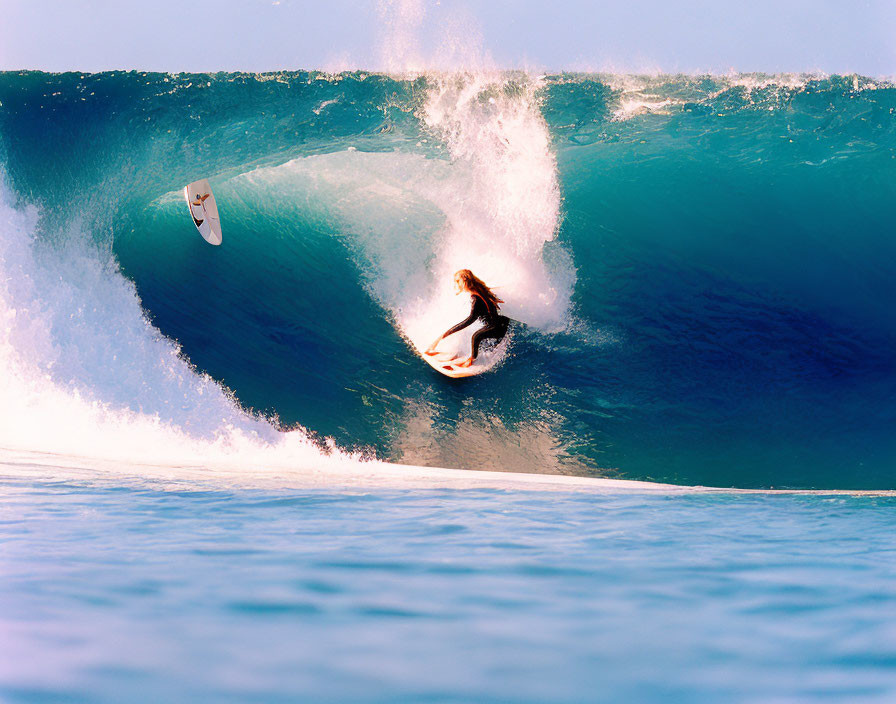 Silhouetted surfer rides blue wave with flying surfboard