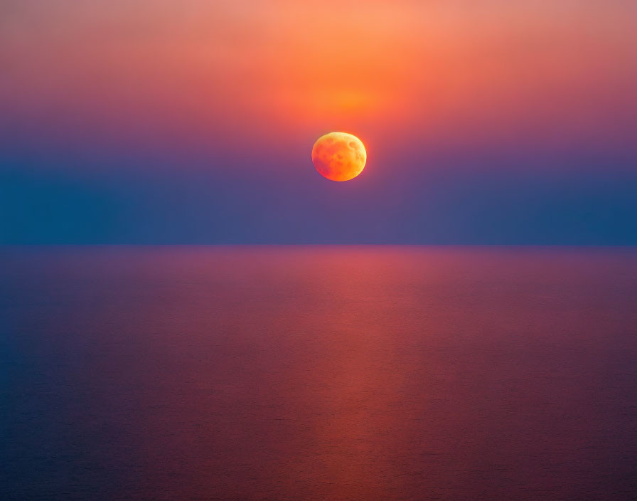 Tranquil sunset scene with large orange sun over calm sea