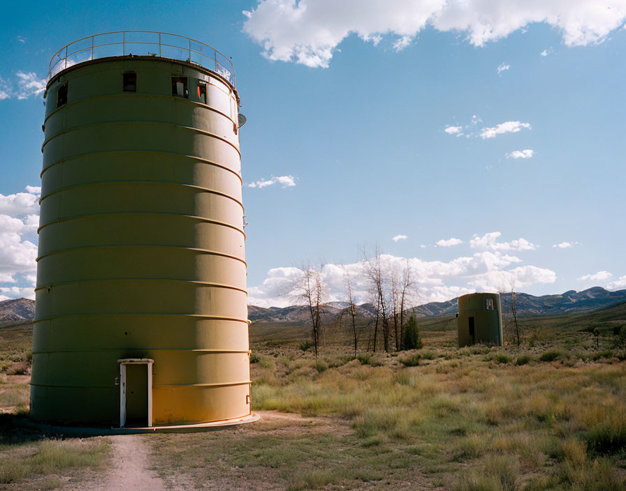 Yellow cylindrical tower next to smaller structure in a field under blue sky.