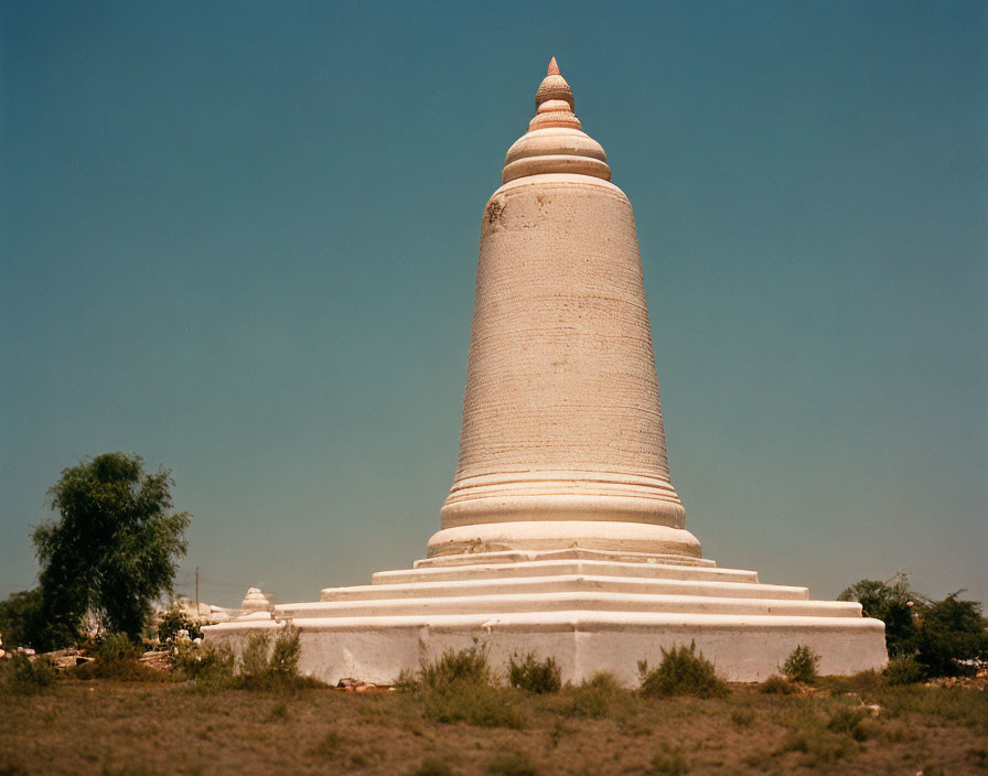 White Stupa with Spiral Tip Amid Greenery and Structures