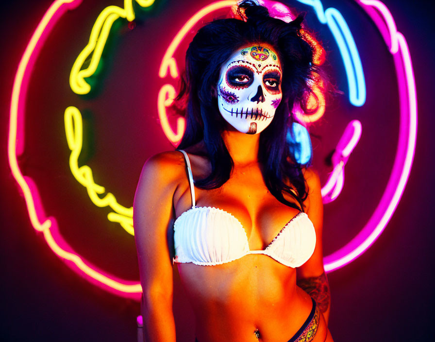 Person with Day of the Dead makeup in front of neon lights with white bra and skull face design.