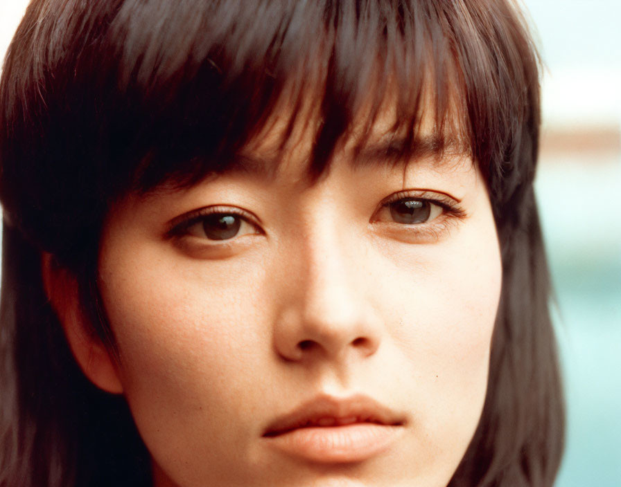 Portrait of woman with dark hair and bangs gazing at camera