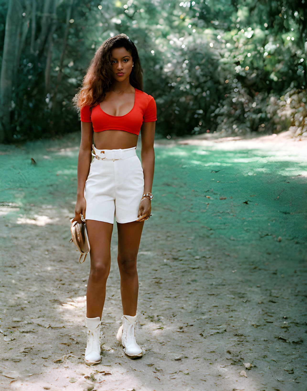 Woman in red crop top and white shorts on sandy path among greenery