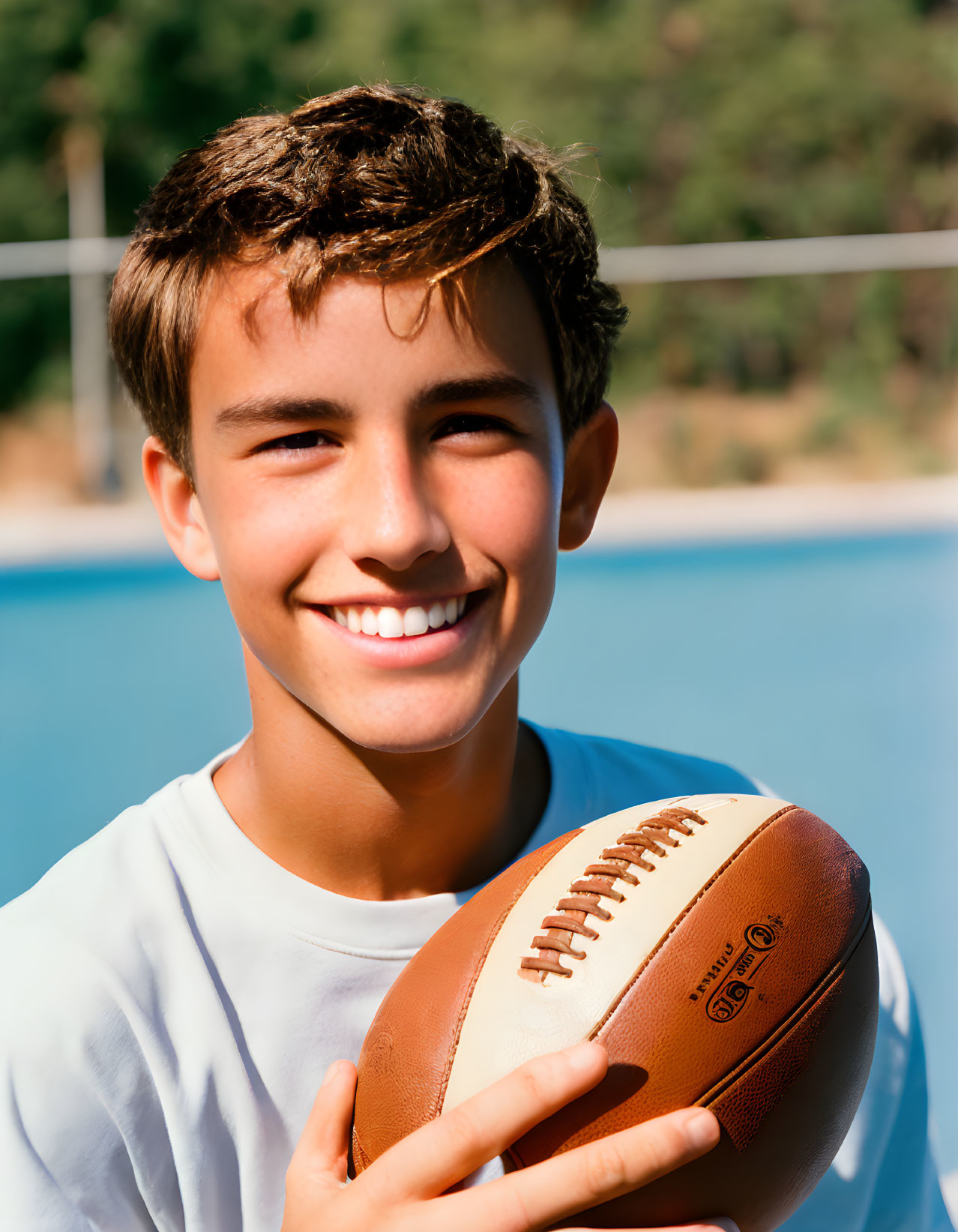 Smiling person with American football by pool & volleyball net