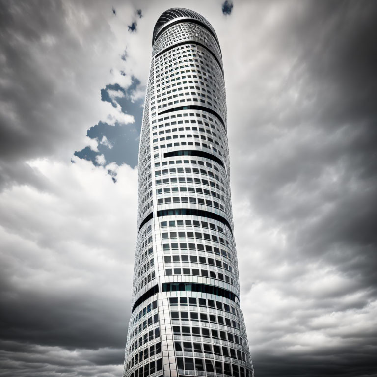 Patterned cylindrical skyscraper under dramatic cloudy sky