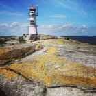 Red and white striped lighthouse on coastal rocks with calm ocean and blue sky