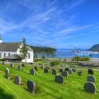 Scenic cemetery and church with white headstones, green landscape, blue skies, snowy mountains