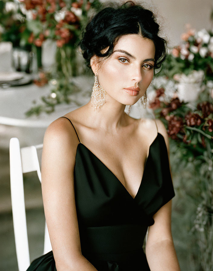 Dark-haired person in black dress and earrings sitting at flower-decorated table.