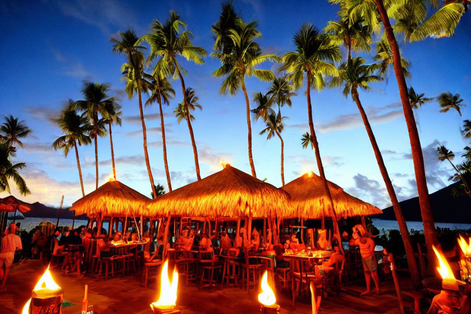 Sunset scene at tropical beach bar with thatched umbrellas, tiki torches, and palm