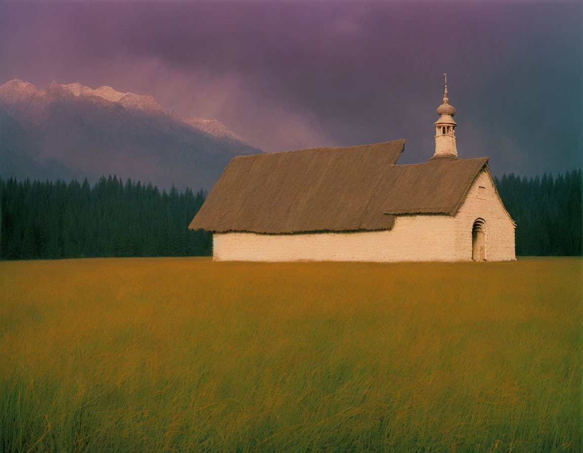 White Thatched Chapel in Golden Field with Forest and Mountains