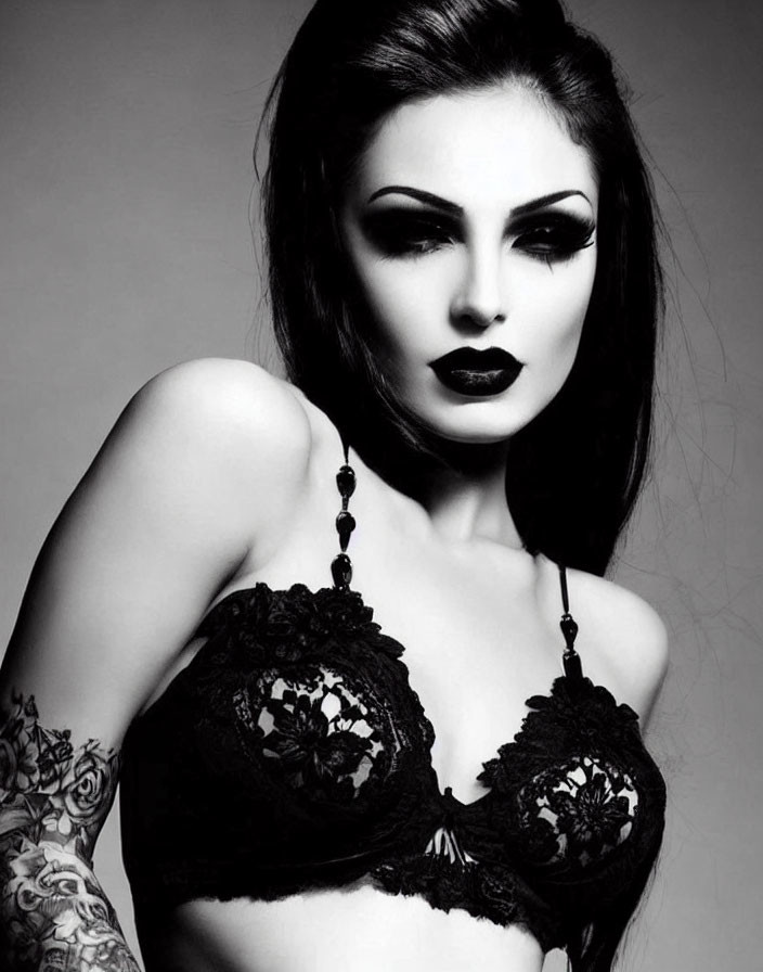 Monochromatic portrait of woman with dark lipstick, winged eyeliner, lace top, and tattoos