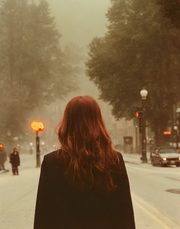 Long Red-Haired Woman on Misty Tree-Lined Street