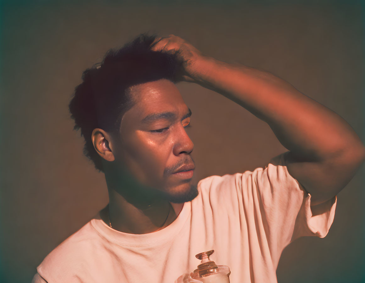 Man in white t-shirt scratching head with bottle under warm light