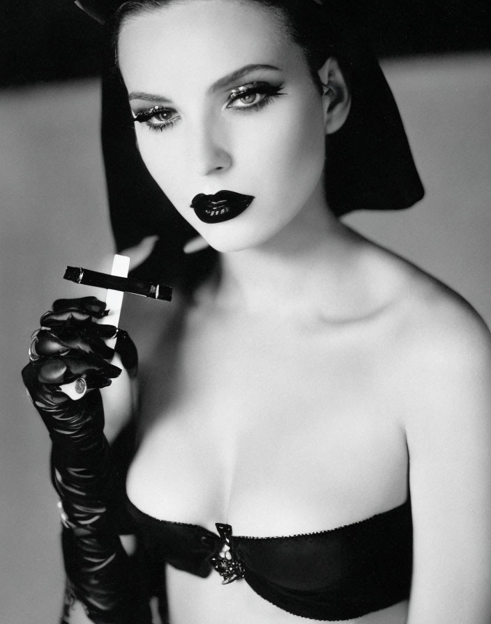 Monochrome portrait of woman with striking makeup and lingerie holding crucifix