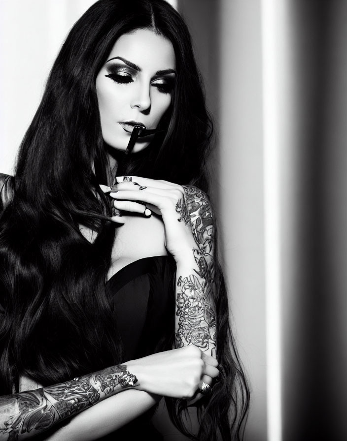 Monochrome portrait of woman with long dark hair and tattoos holding pen