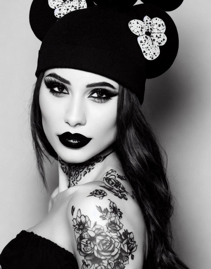 Portrait of woman with strong makeup and cartoon mouse ear beanie, floral tattoos in black and white