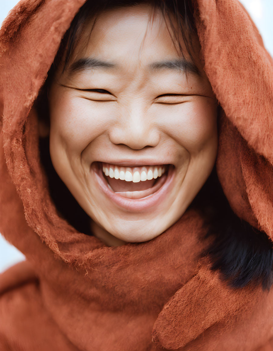 Person with big smile wearing rust-colored hood in joyful expression.