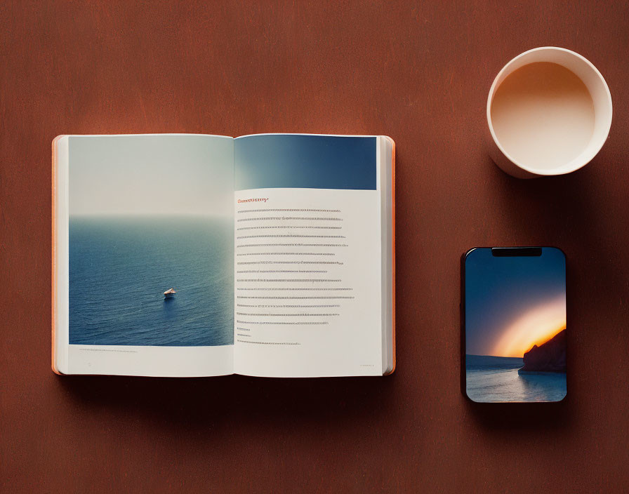 Open book with boat image, text, cup, and smartphone on brown surface