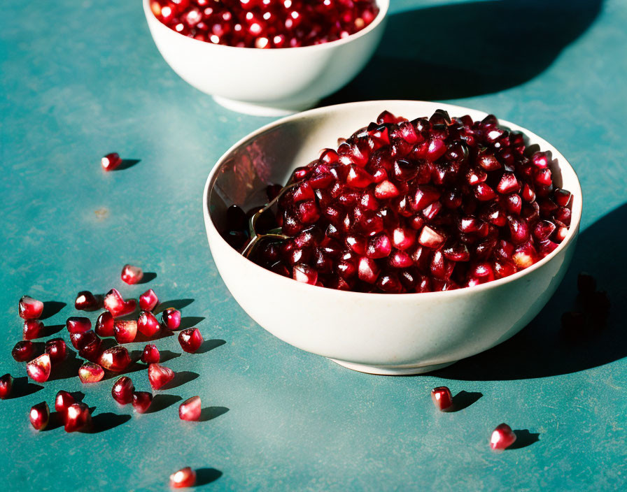 White bowls with pomegranate seeds on teal surface