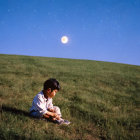 Young boy sitting on grassy hill under twilight sky with stars and moon.