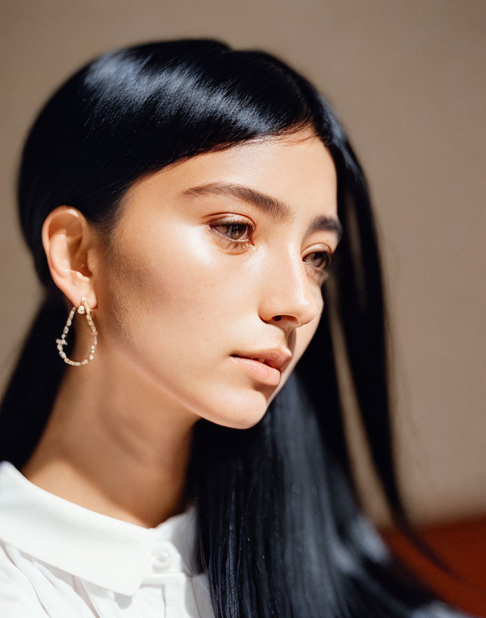 Profile view of person with long black hair, hoop earrings, and white top in sunlight.