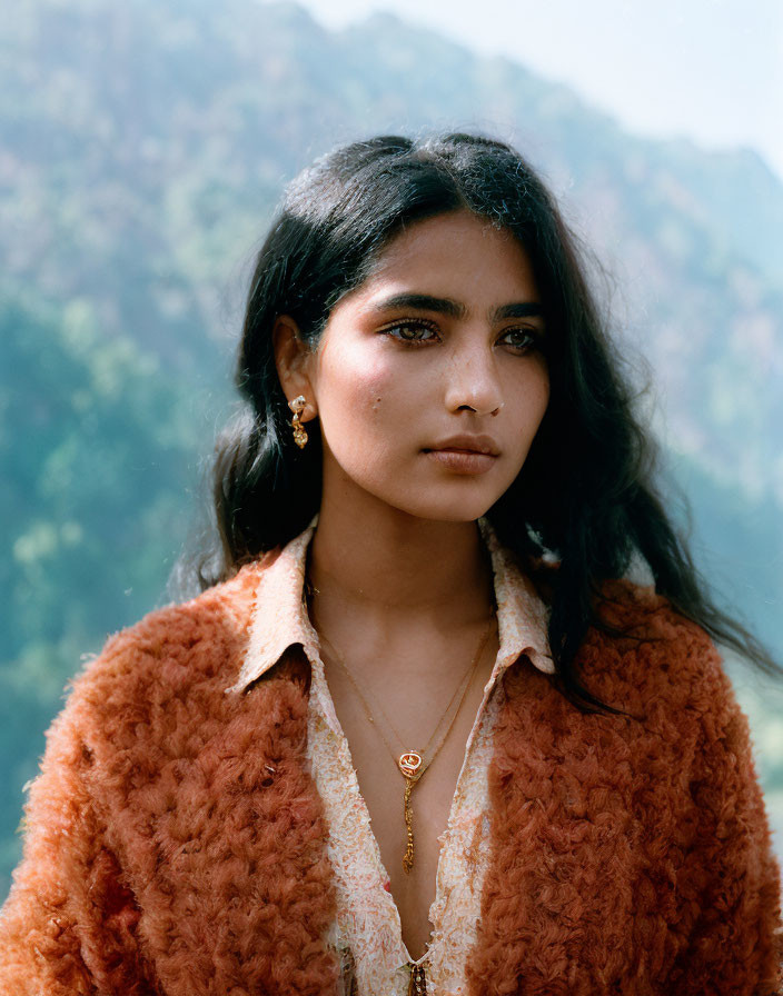 Dark-haired woman in brown fluffy jacket and pendant necklace outdoors