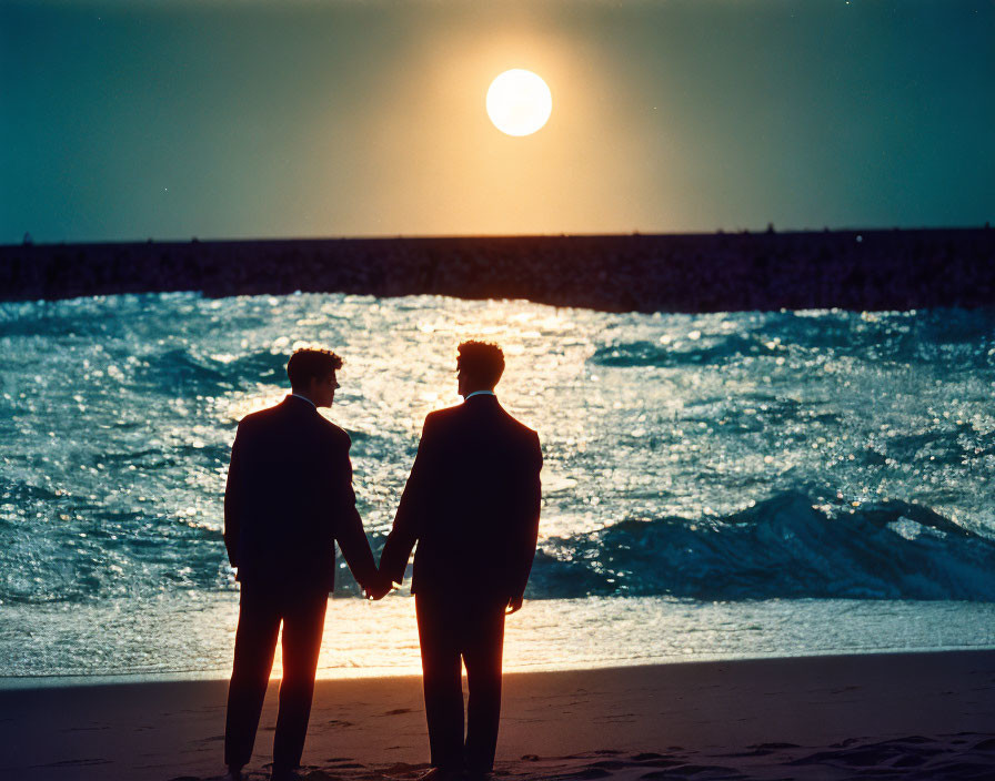 Couple holding hands on beach at sunset with waves and low sun