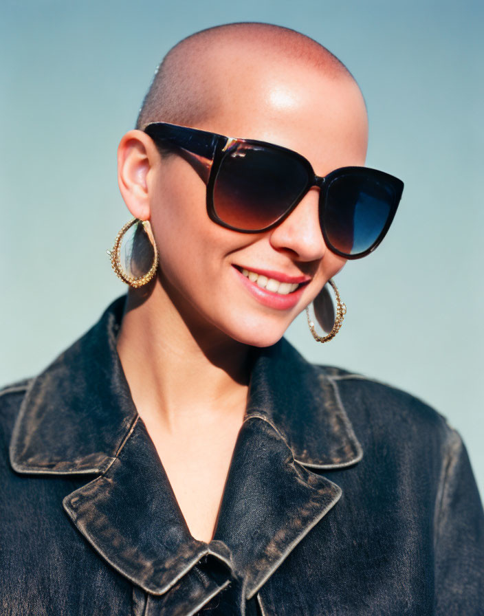 Bald person in sunglasses and hoop earrings under clear blue sky