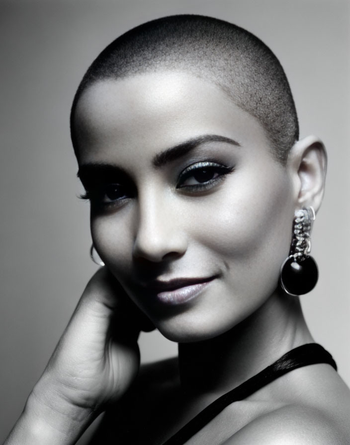 Portrait of woman with shaved head and earring, gazing at camera with subtle smile