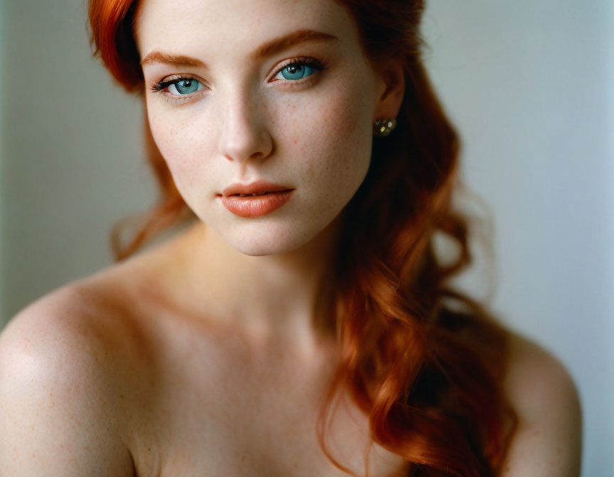 Portrait of woman with red hair, green eyes, freckles, makeup, and earrings.