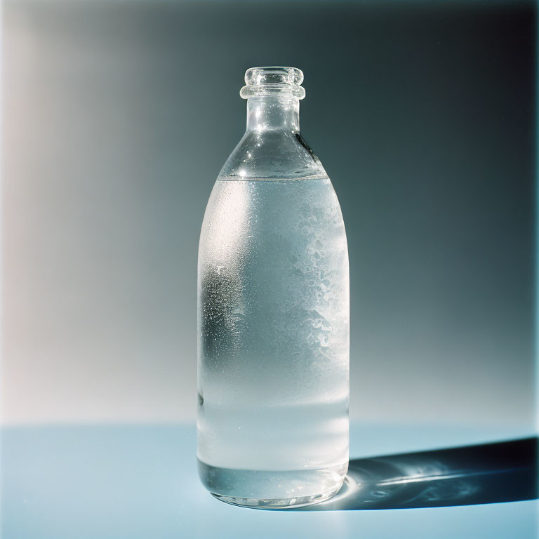 Clear glass bottle with cold water on light blue gradient background