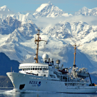 Large ship sailing icy mountainous waters with snow-capped peaks under blue sky