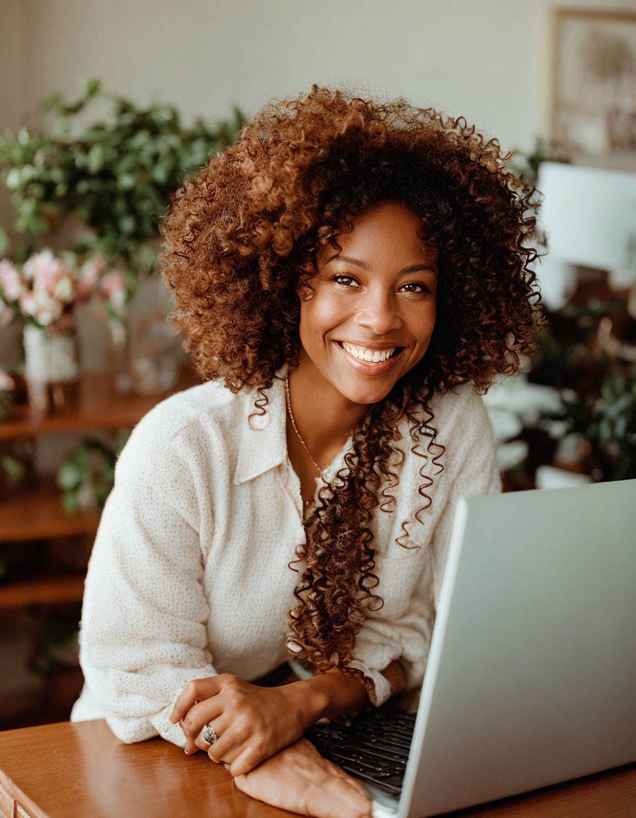 Curly-Haired Woman Smiling at Desk with Laptop and Plants