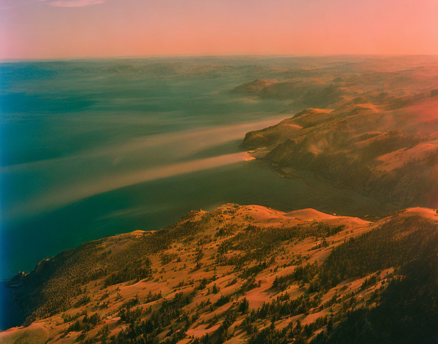 Hilly Coastline Over Smooth Water Under Warm Hazy Sky