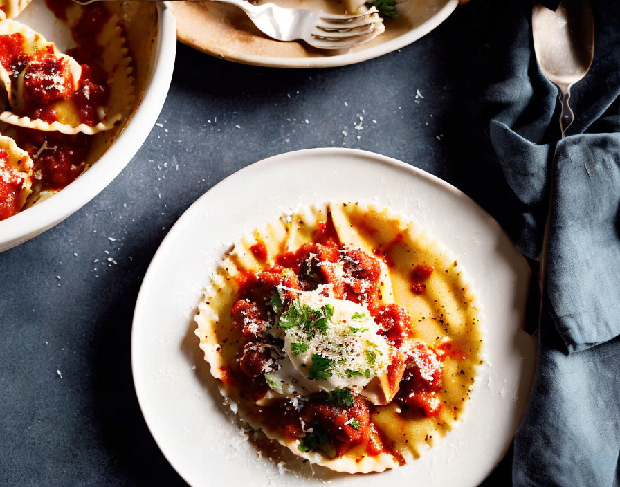 Plate of ravioli with tomato sauce, meatballs, and cheese on dark table