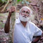 Elderly man with white beard and blue eyes in woods portrait.