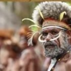 Traditional tribal attire with colorful beads and feathers in front of thatched huts.