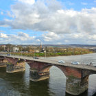 Historical stone bridge over river with vehicles, cityscape, trees, old buildings under cloudy sky