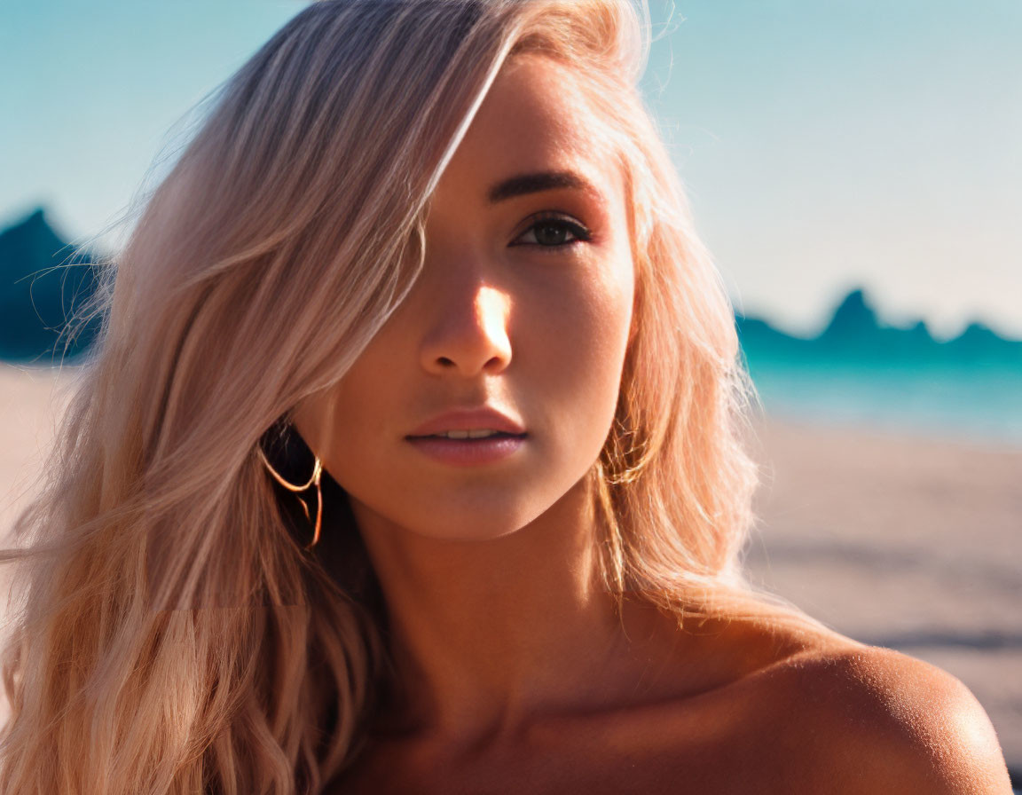 Blonde woman with hoop earrings on beach backdrop.