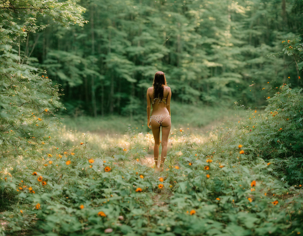 Woman in bikini surrounded by wildflowers and green forest