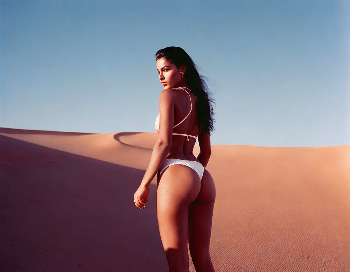 White swimwear model poses on sandy desert dune under blue sky