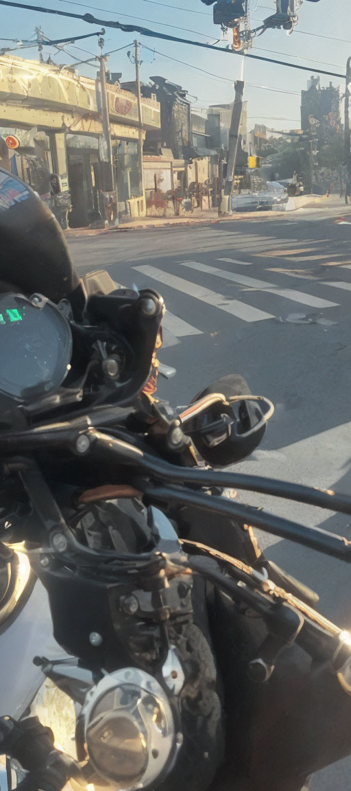 Motorcycle cockpit view at street intersection with traffic and buildings on sunny day