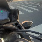 Motorcycle cockpit view at street intersection with traffic and buildings on sunny day