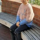 Short-haired animated female character in fur vest, blue top, and black pants on wooden bench in natural