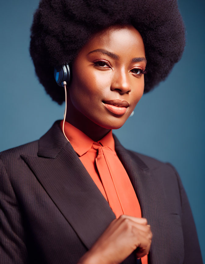 Woman with Afro Hair in Black Blazer and Orange Shirt on Blue Background