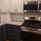 Modern kitchen with dark blue cabinets, wooden countertops, bar stools, pendant lights, and greenery.