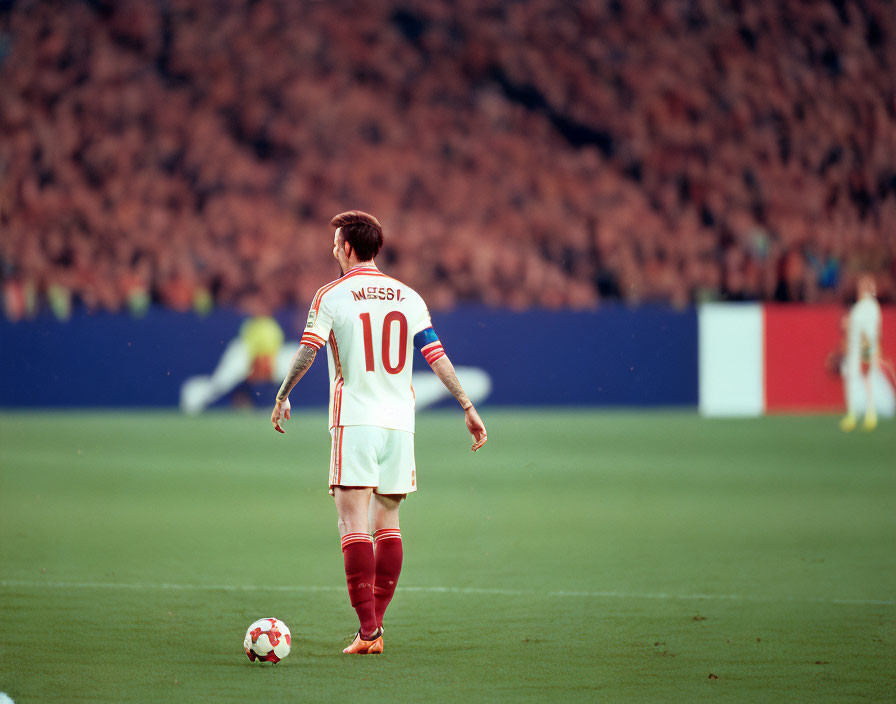 Soccer player in number 10 jersey on field with ball, facing stadium crowd