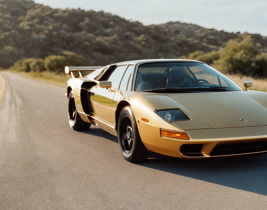 Gold Lamborghini Countach with scissor doors parked on empty road at golden hour