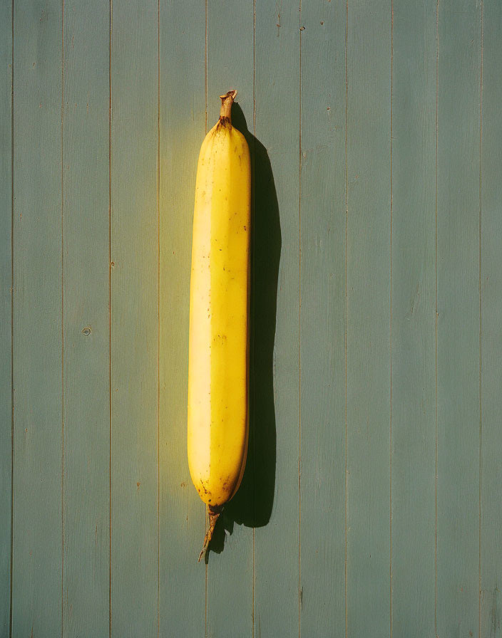 Ripe banana with blemishes on green wooden surface in warm light