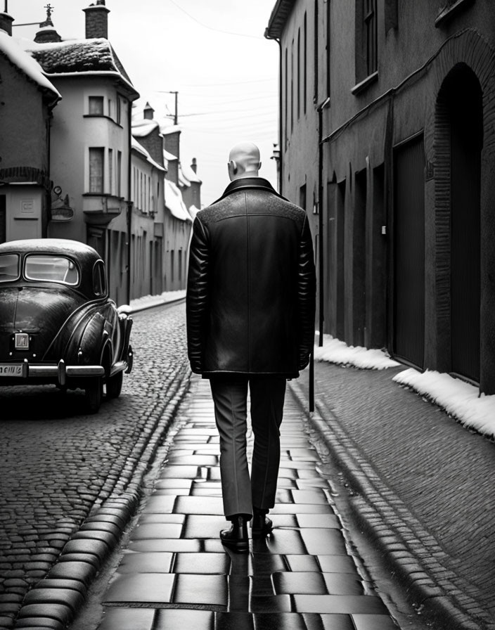 Person in leather jacket walking by vintage car on cobblestone street